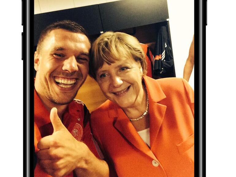 Nach dem WM-Auftaktsieg gegen Portugal posiert Merkel in der deutschen Kabine mit der Mannschaft und wird danach zwanglos von Lukas Podolski am ausgestreckten Arm abgelichtet.