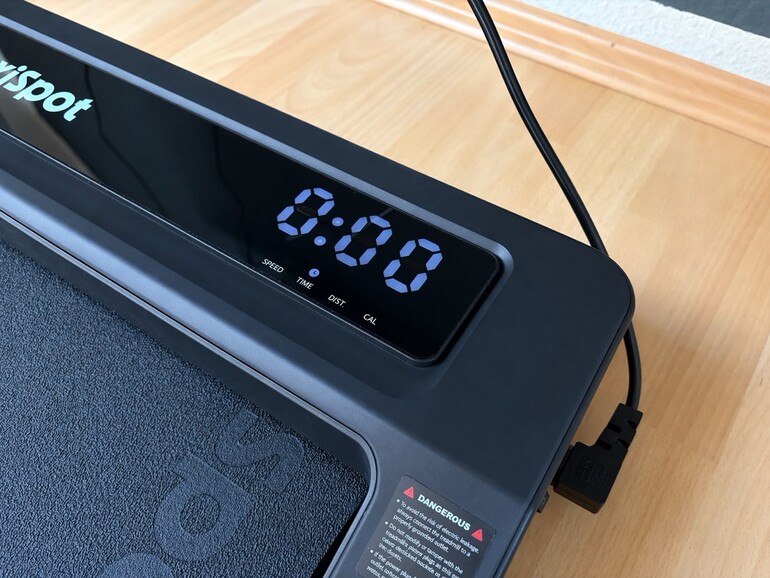Das Display zeigt Tempo, Zeit, Distanz und Kalorien. Das Stromkabel sitzt seitlich und bleibt im Alltag sichtbar.