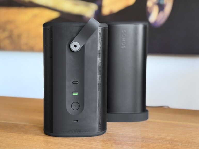 Rückansicht des Duos: Die Trageschlaufe klappt flach weg, wenn man sie nicht braucht. Gut sichtbar: der Hardware-Mikrofon-Schalter (grün = aktiv), der Einschalter und der USB-C-Anschluss.
